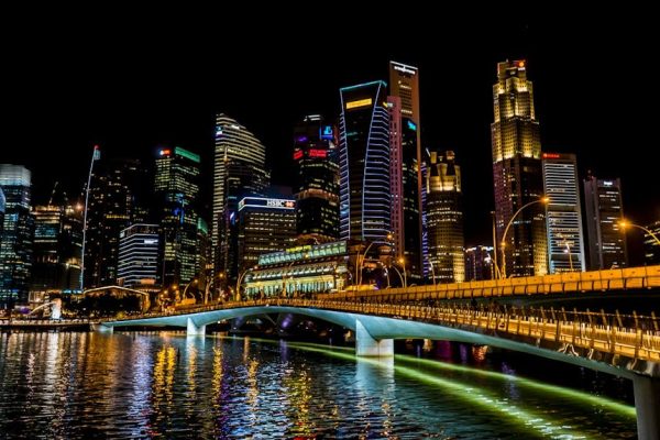 Stunning Singapore cityscape featuring vibrant skyscrapers, illuminated bridge, and reflections over the river at night.