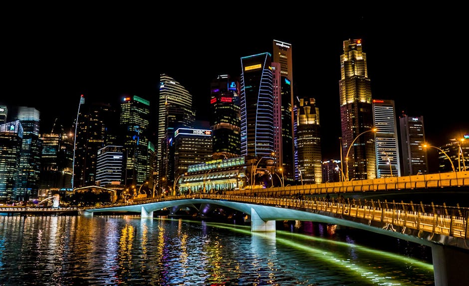Stunning Singapore cityscape featuring vibrant skyscrapers, illuminated bridge, and reflections over the river at night.