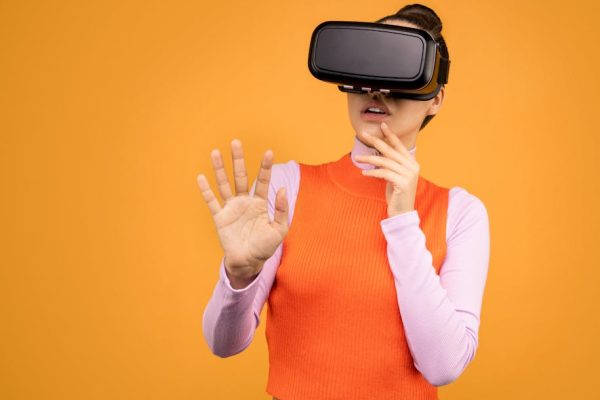 Woman with VR headset exploring an immersive virtual reality experience on an orange background.