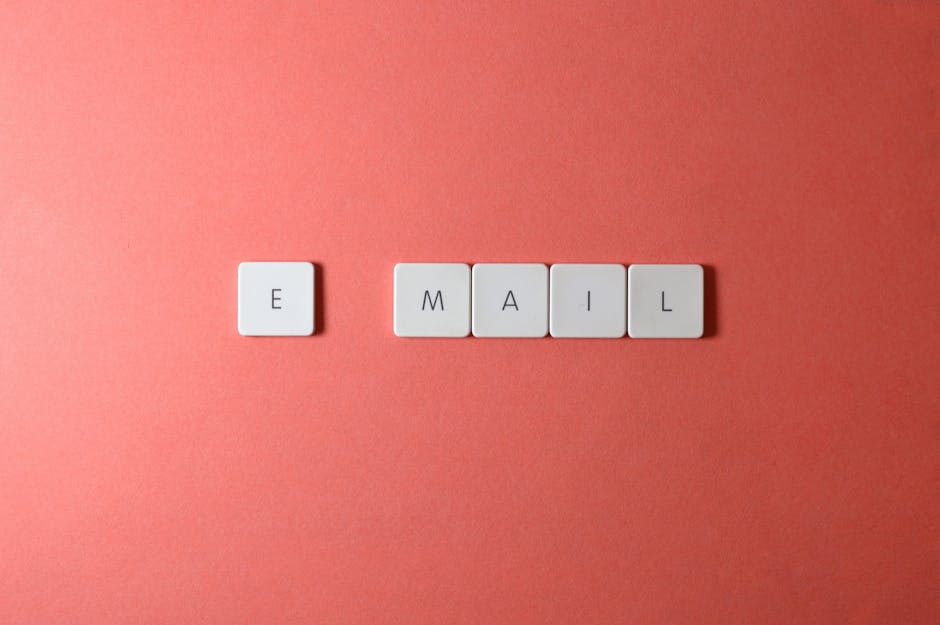 Flat lay of keyboard letter tiles spelling 'email' on coral backdrop.