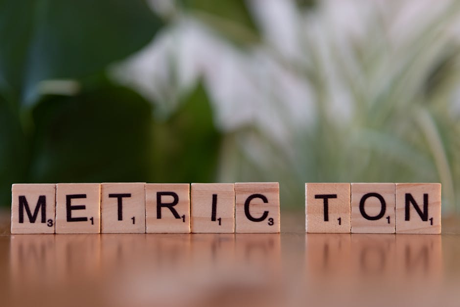 Scrabble tiles on a brown surface spell 'Metric Ton' with blurred green background.