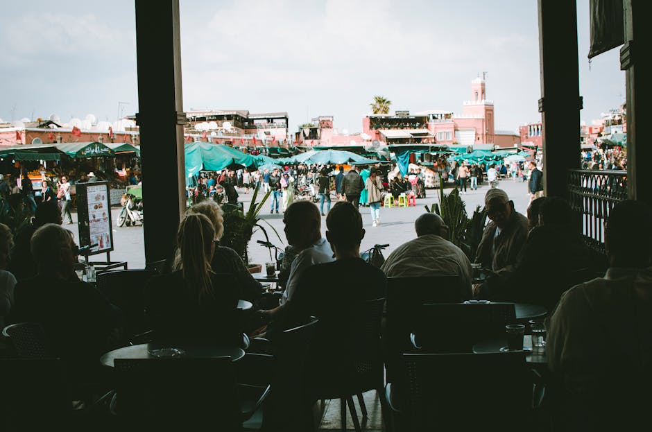 A vibrant Moroccan market filled with people, seen from a shaded cafe.
