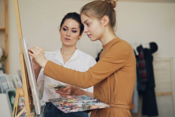 Two women engaged in painting and learning art techniques in a studio setting.