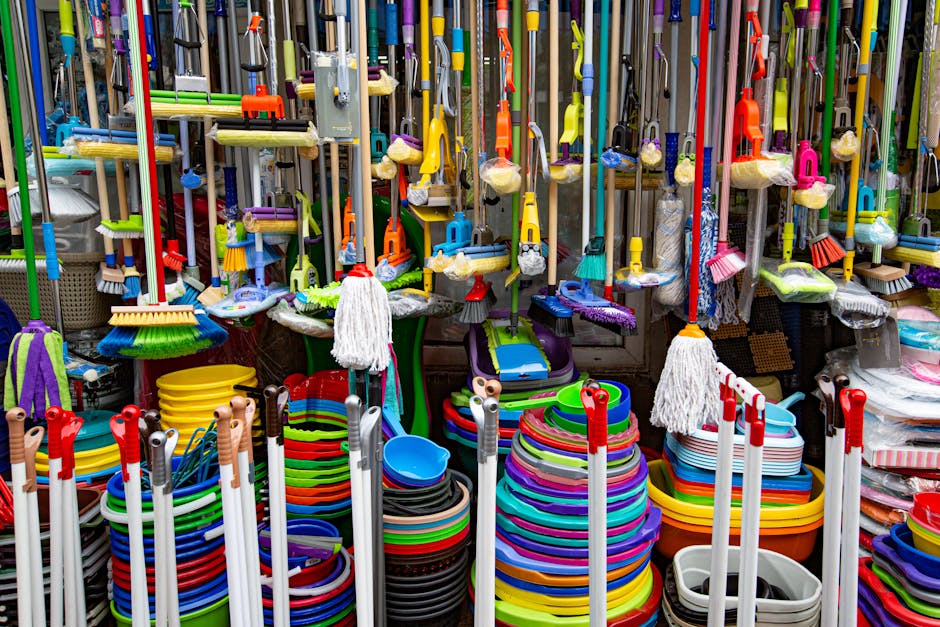Various colorful mops and brushes arranged with stack of plastic basins and bins in household goods supermarket