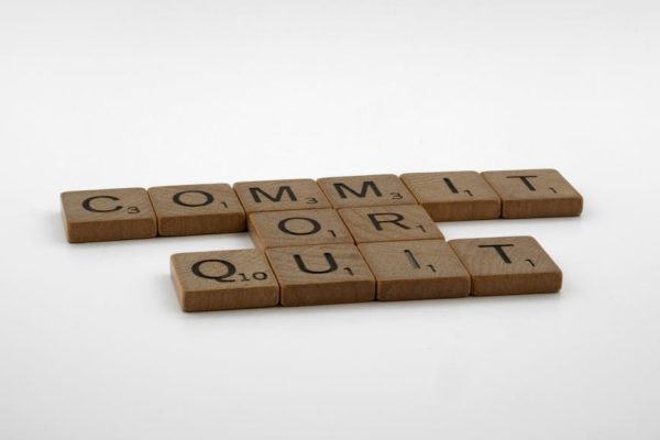 Scrabble tiles spelling 'Commit Or Quit' on a white surface, symbolizing decision-making.
