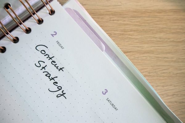 Top view of a notebook open to a day planner featuring 'Content Strategy' handwritten, lying on a wooden desk.