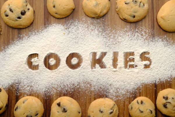 Freshly baked chocolate chip cookies arranged on flour-dusted wooden table.
