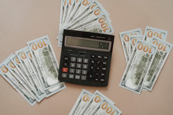 Top view of a calculator showing $5200 surrounded by $100 bills on a tan background.