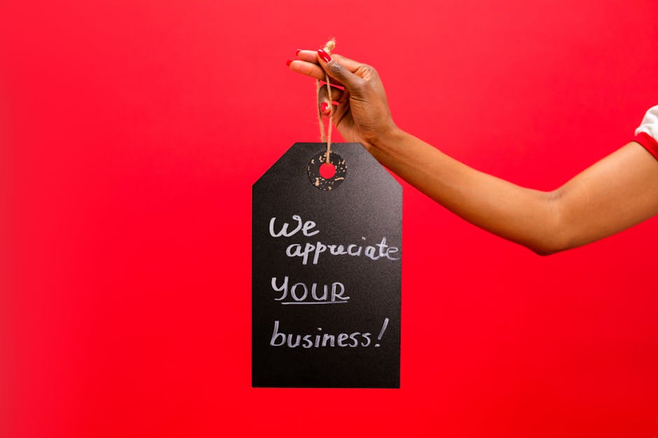 A hand holding a thank you sign with 'We appreciate your business!' on a red backdrop.
