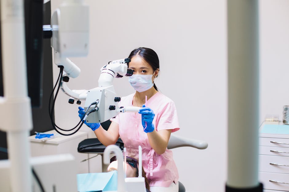 A female dentist wearing a mask uses a microscope in a dental clinic setting for precision treatment.