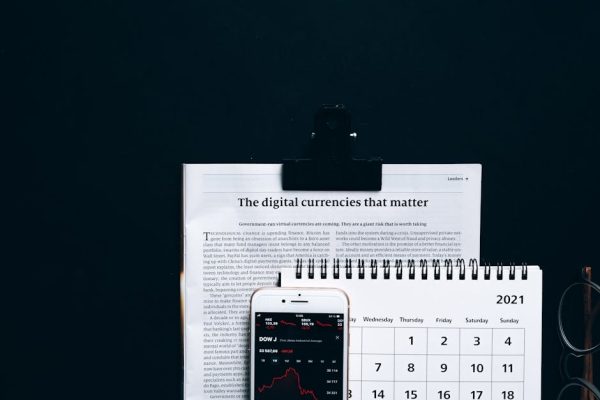 Digital currencies article with smartphone stock market app and calendar on black surface.