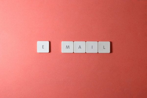 Flat lay of keyboard letter tiles spelling 'email' on coral backdrop.