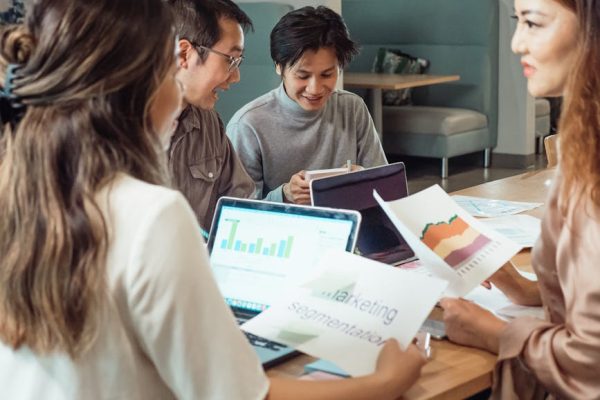 Group of colleagues discussing marketing strategies with charts and laptops in an office setting.