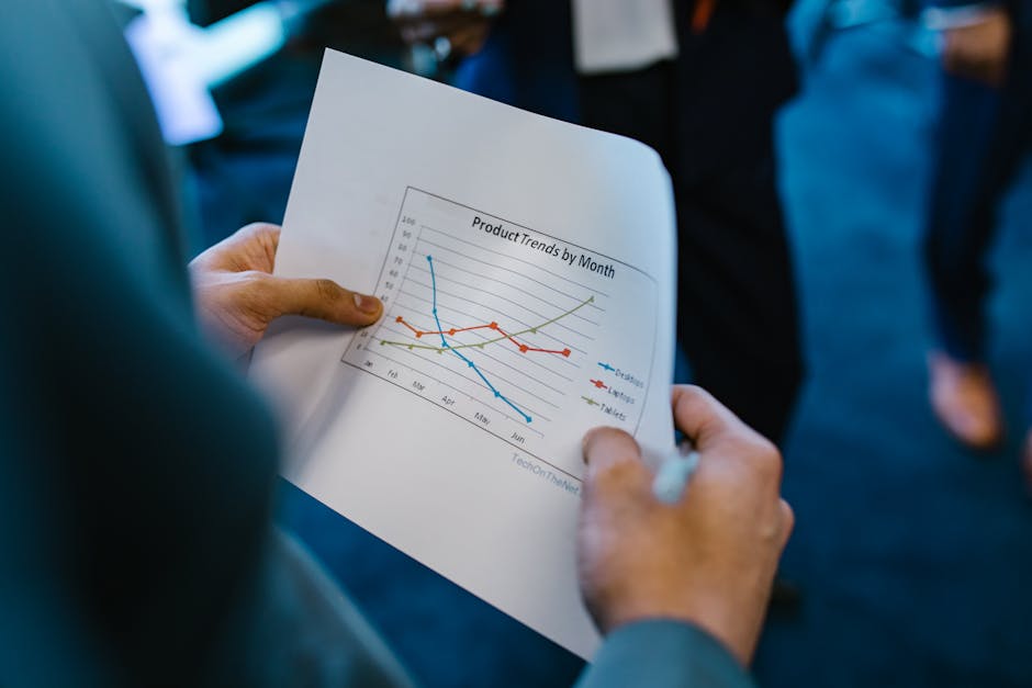 Close-up of hands holding a paper with a line graph showing product trends by month during a business meeting.