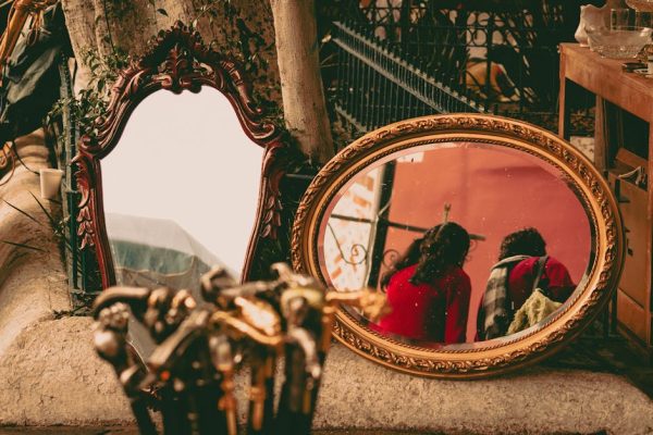 Ornate vintage mirrors at an outdoor market reflecting two women in colorful attire.