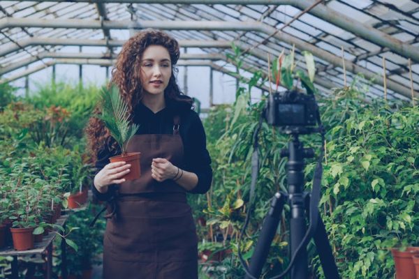 Young woman filming a plant care tutorial inside a lush greenhouse.