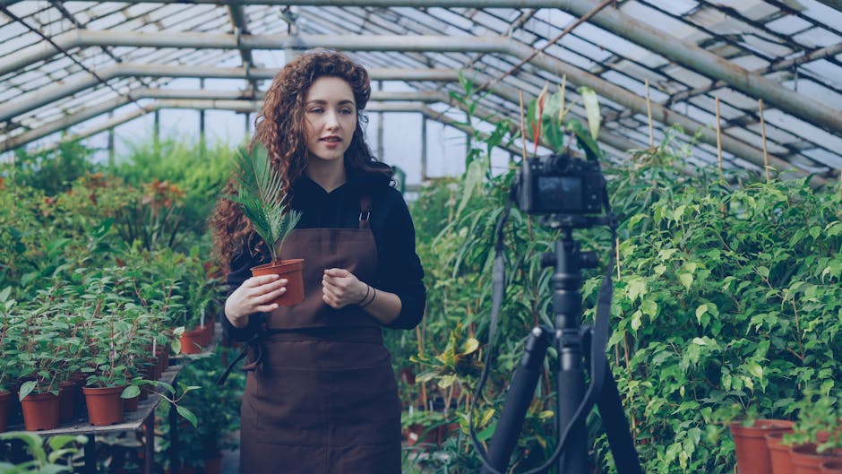 Young woman filming a plant care tutorial inside a lush greenhouse.