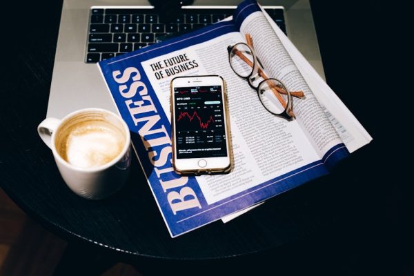 A business setup with a laptop, coffee, phone, and newspaper. Perfect for finance themes.