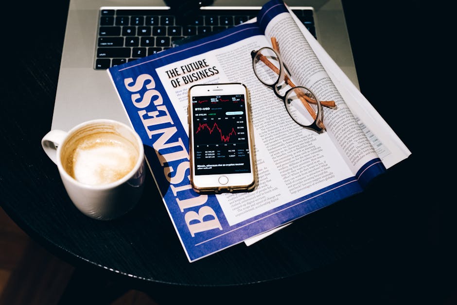 A business setup with a laptop, coffee, phone, and newspaper. Perfect for finance themes.