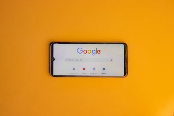Smartphone displaying Google search page on a vibrant yellow background.
