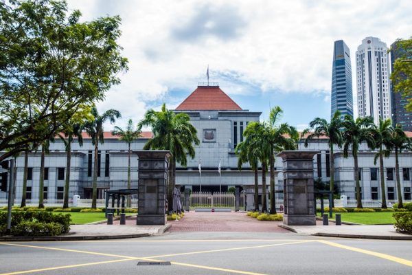Exterior view of Singapore Parliament House with lush greenery and skyscrapers in the background.