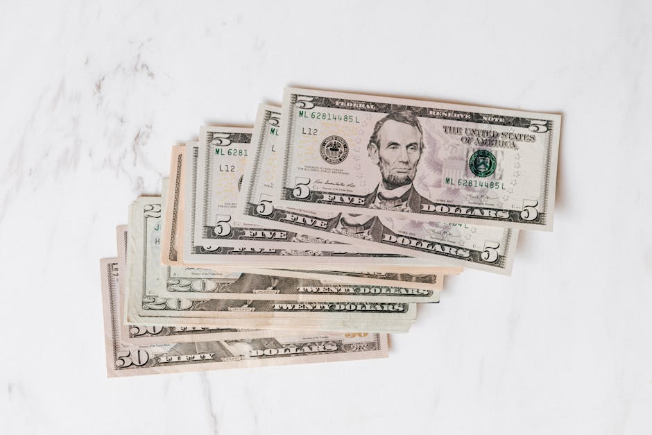 Stack of various US dollar bills on a clean marble surface, emphasizing finance and currency.