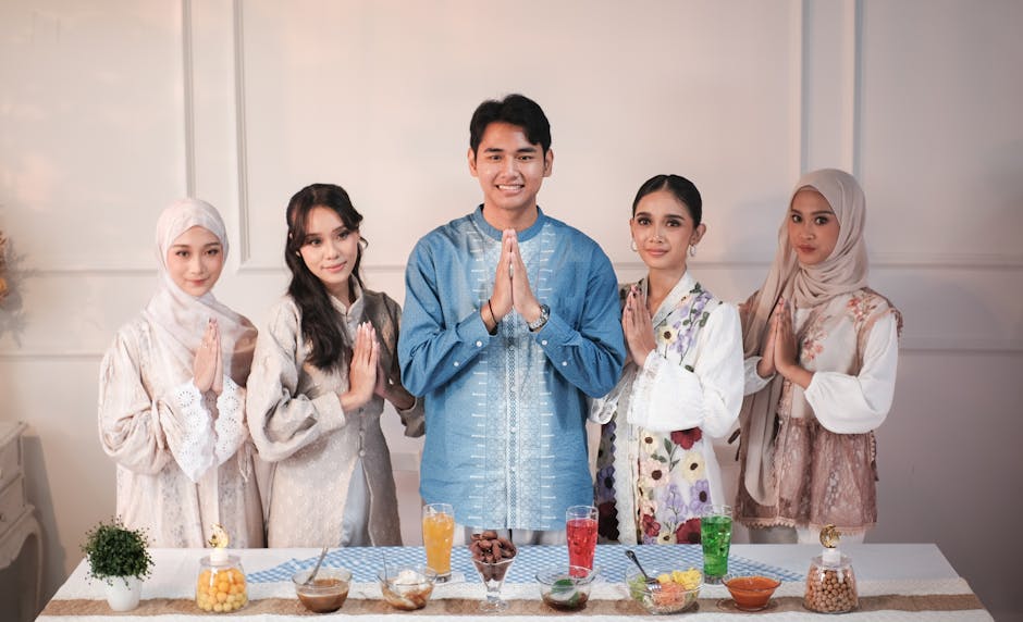 Five individuals in traditional attire celebrating Eid with hands in prayer position over a table with food.