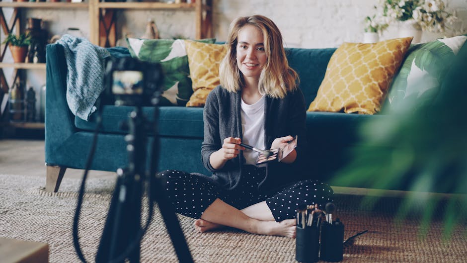 Smiling woman filming a makeup tutorial indoors with brushes and camera setup.