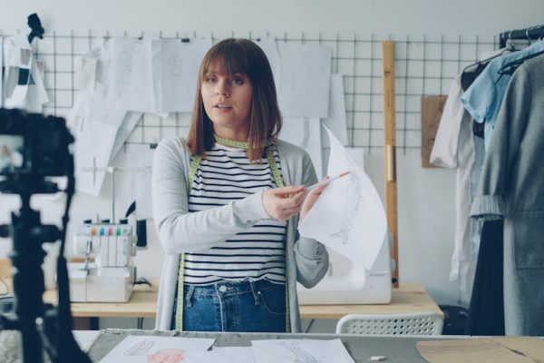 Female fashion designer explaining her sketches on camera in a studio setup.