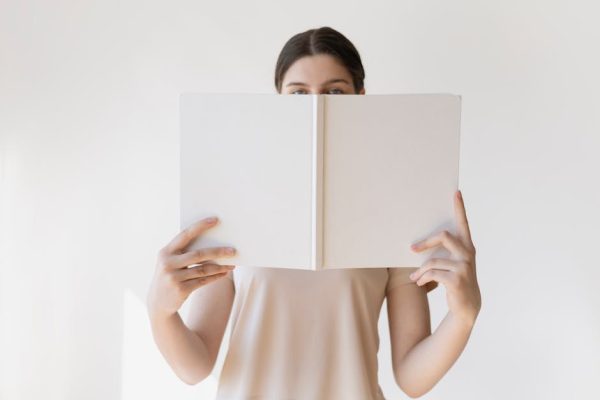 A young woman holds a blank book in front of her face, ideal for mockup purposes.