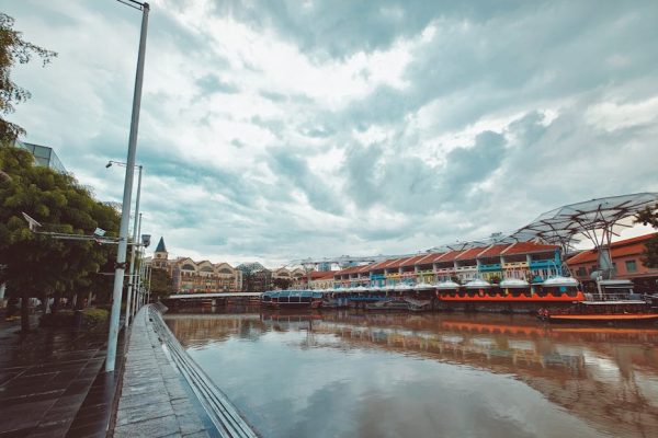 Vibrant boats docked at Clarke Quay in Singapore under a dramatic cloudy sky.