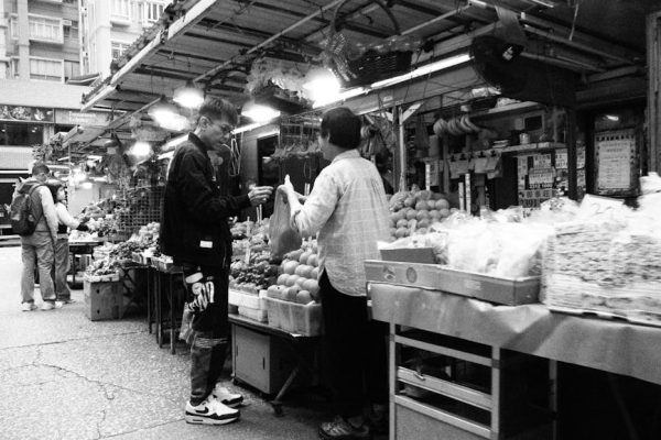 Capturing a candid interaction at a bustling Hong Kong street market in black and white.