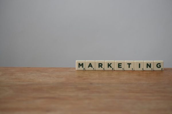 Scrabble tiles spelling 'MARKETING' on a wooden table with a neutral background.