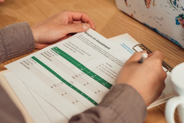 A person analyzing a return on investment report with a pen in hand on a desk.