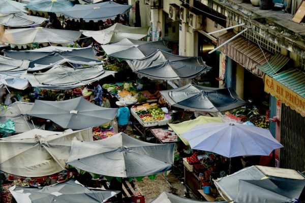 Vibrant outdoor market scene viewed from above with numerous stalls and umbrellas.