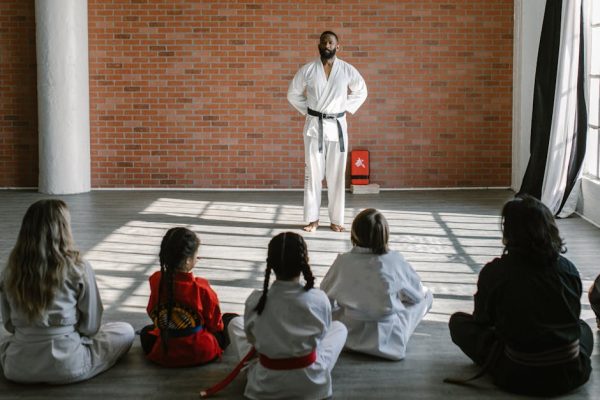 Young students in gis learn martial arts under the guidance of a black belt sensei in a dojo setting.