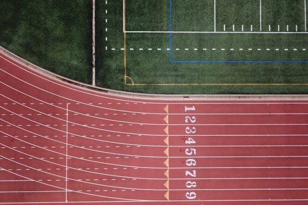 Aerial perspective of a red running track and adjacent green field.