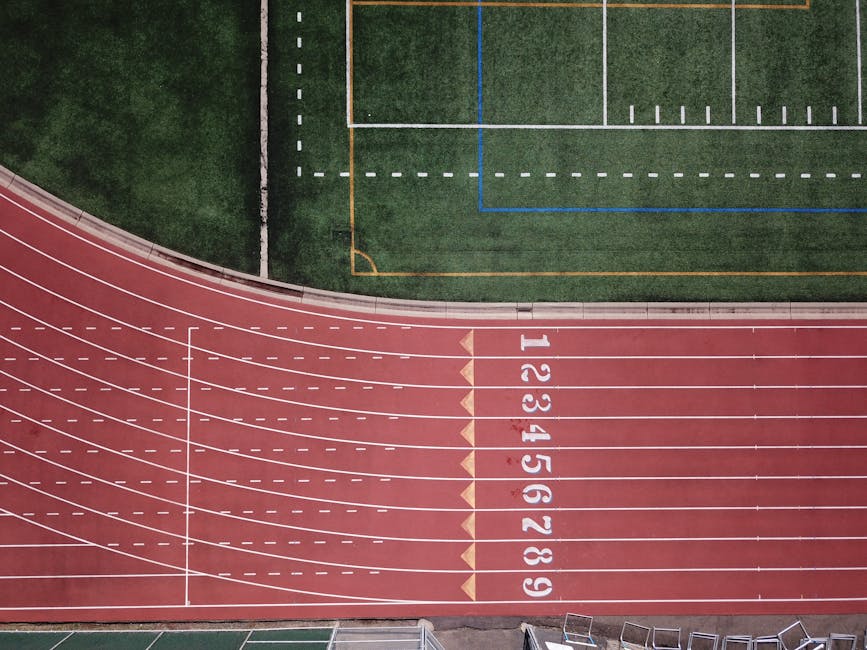 Aerial perspective of a red running track and adjacent green field.