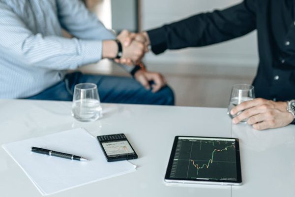 Business meeting with handshake and financial analysis displayed on a tablet.