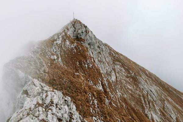 A dramatic mountain peak shrouded in fog, showcasing rugged rocky terrain.