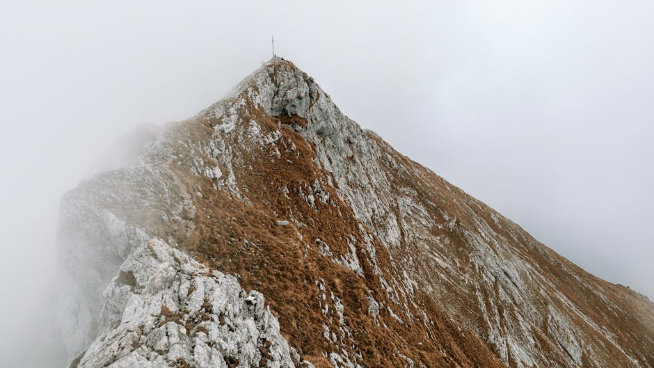 A dramatic mountain peak shrouded in fog, showcasing rugged rocky terrain.