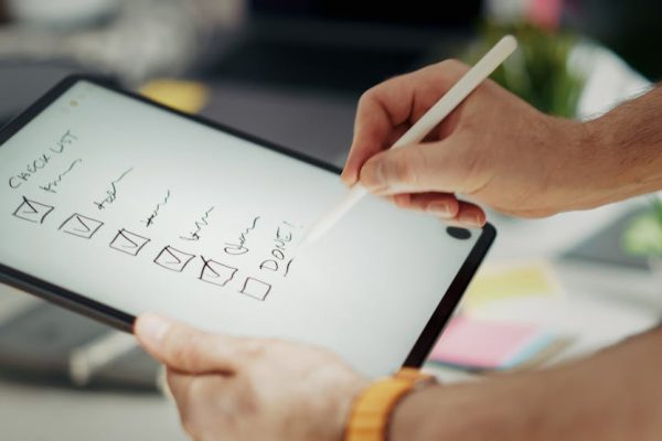 Close-up of a hand writing on a digital checklist using a stylus on a tablet, enhancing productivity.