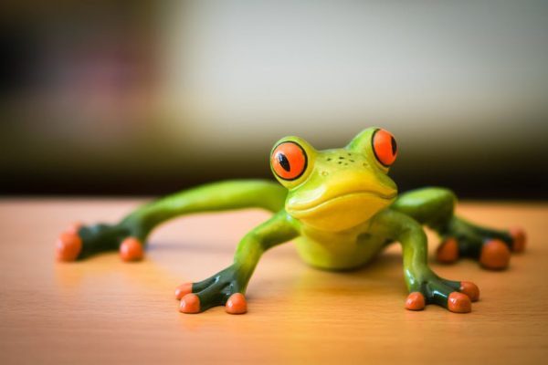 Vibrant green frog figurine with striking orange eyes and toes on a wooden surface.