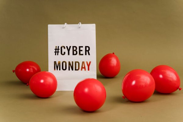 Shopping bag with hashtag Cyber Monday surrounded by vibrant red balloons.