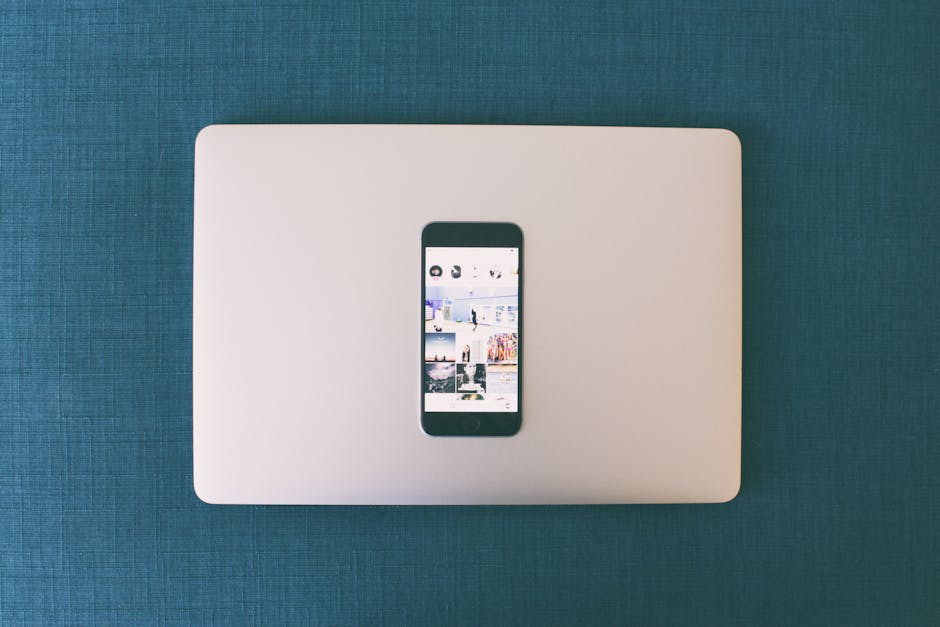 Flat lay of a smartphone on a laptop with social media photos on screen.