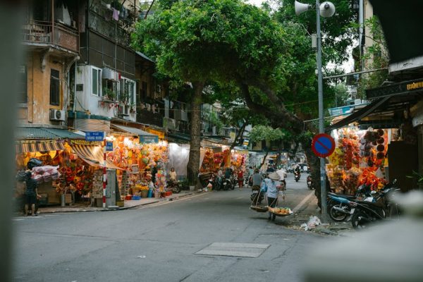 Street market in Hanoi, Vietnam with vendors and shoppers, vibrant lights, and motorbikes at dusk.