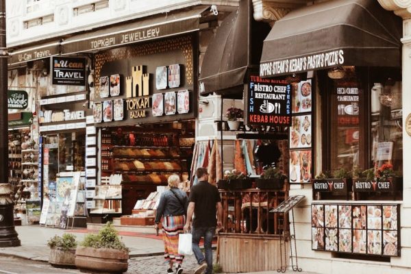 Couple walking through a lively city bazaar street lined with shops and eateries during the day.