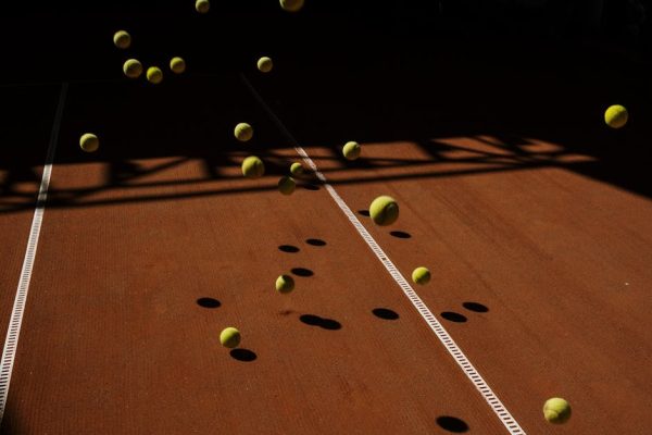 Artistic capture of tennis balls in motion casting dramatic shadows on a clay court surface.