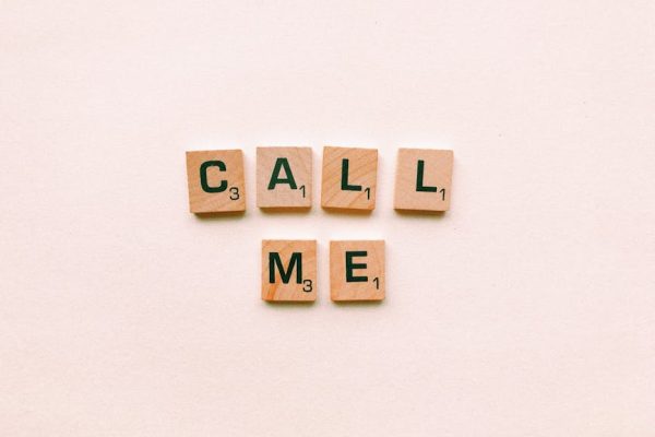 Wooden letter tiles spelling 'Call Me' on a pastel pink background, invoking communication and connection.