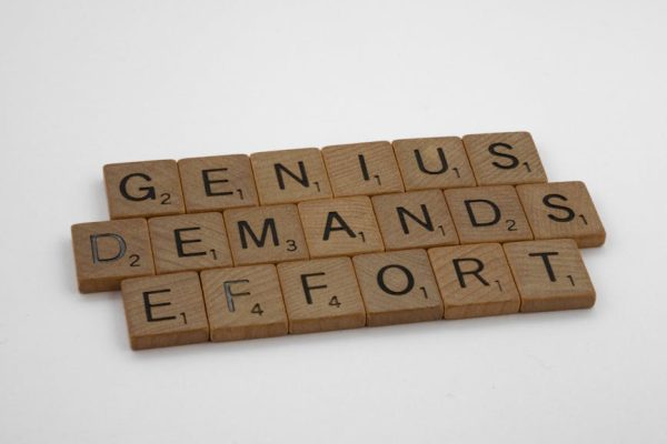 Scrabble tiles spelling 'Genius Demands Effort' on white surface, highlighting creativity and persistence.